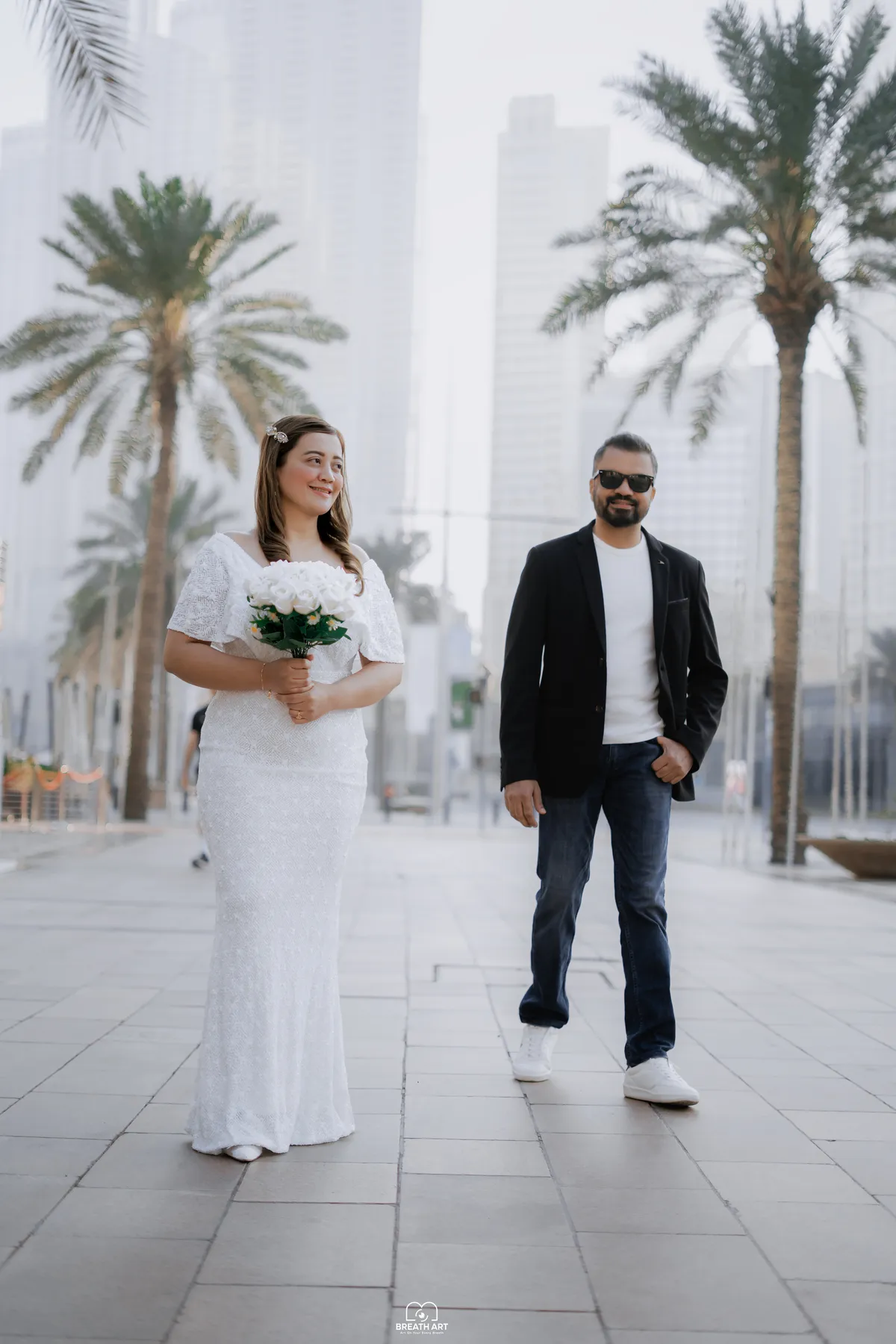 Couple walking between palm trees in Downtown Dubai during a BreathART pre-wedding shoot