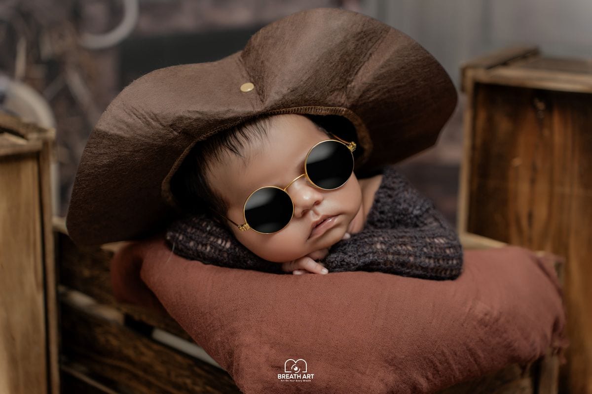 Newborn baby in a cowboy hat and sunglasses costume