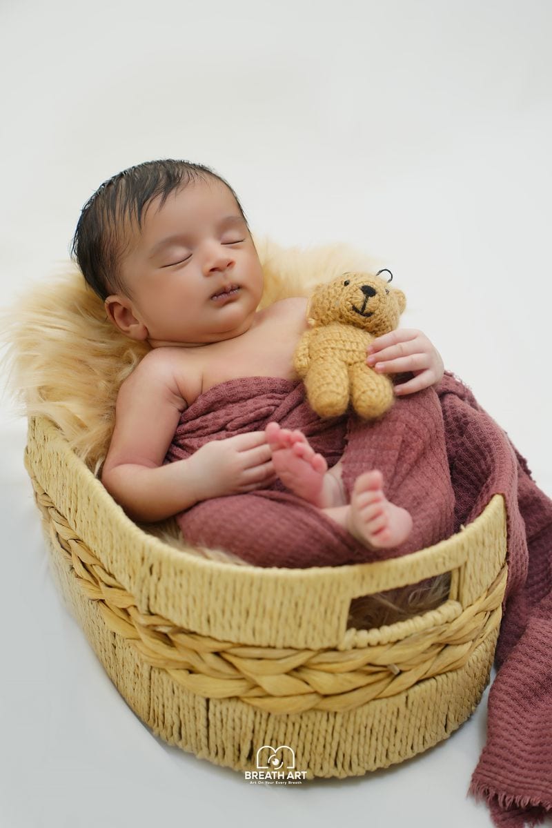 Newborn baby in a basket with a teddy bear